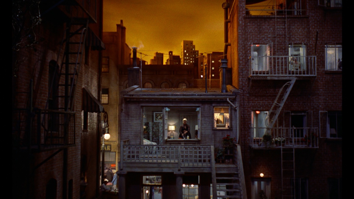A cinematic nighttime cityscape from Alfred Hitchcock’s Rear Window (1954), featuring meticulously designed apartment exteriors, fire escapes, and warm lighting, showcasing Hal Pereira’s masterful art direction.