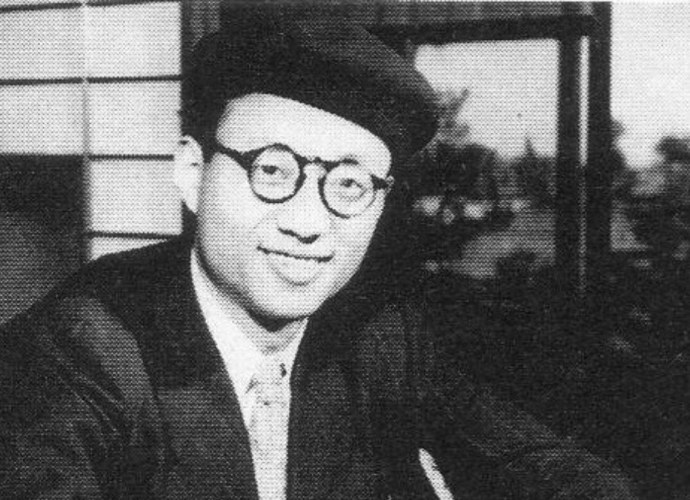 Black and white portrait of Osamu Tezuka wearing a beret and round glasses, smiling at the camera.