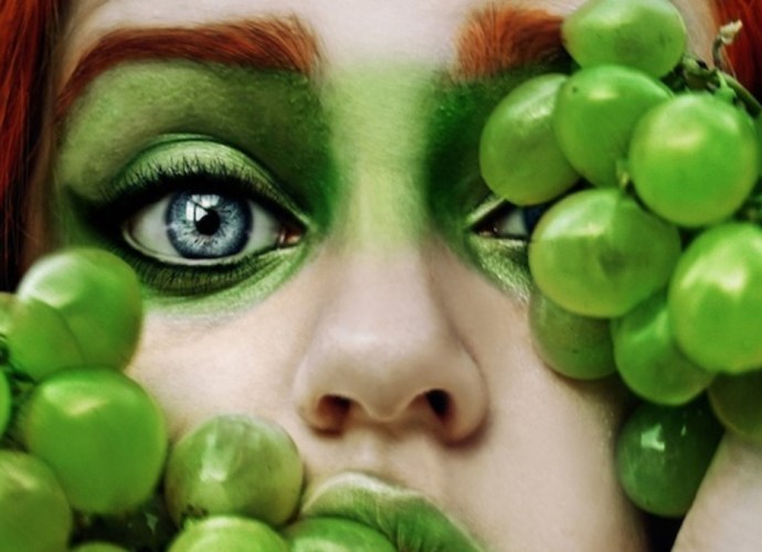 ortrait of a woman with green makeup and red hair holding green grapes, blending surrealism with nature."