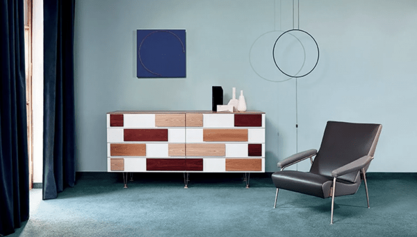 A modern interior featuring Gio Ponti-inspired furniture, including a geometric wooden sideboard with white, red, and natural wood panels, a sleek black lounge chair, and minimalist wall decor.