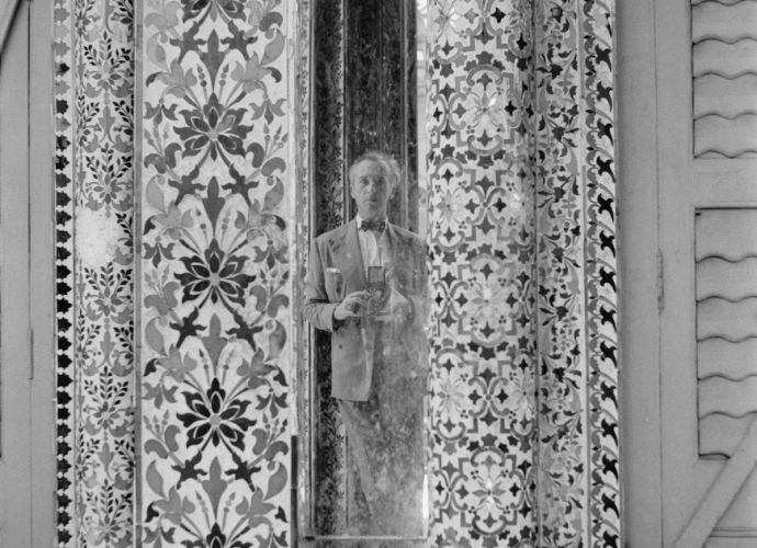 Cecil Beaton in a civilian suit holding his Rolleiflex camera, reflected in a mirror of the Jain temple in Calcutta, India.
