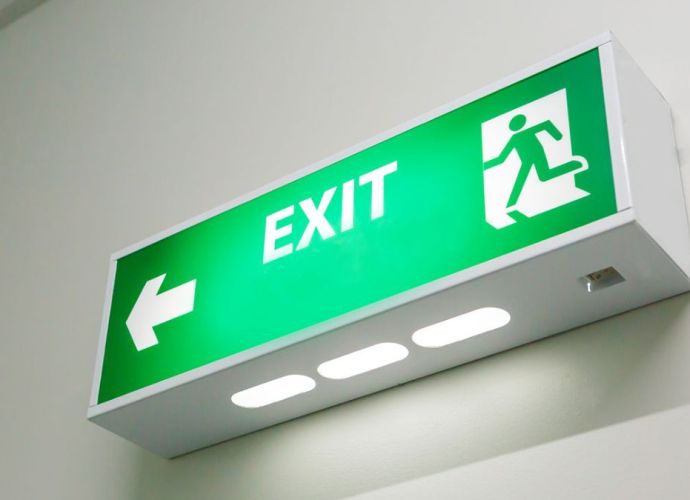 Illuminated green exit sign with a directional arrow and running figure, mounted on a wall.