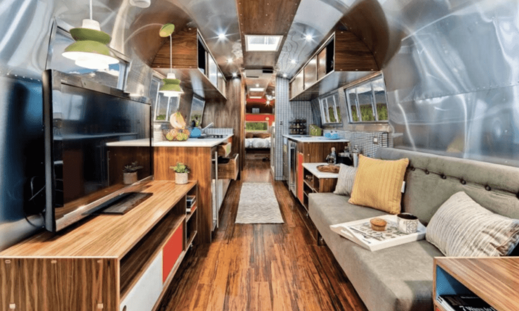 A stylishly restored 1962 Airstream interior featuring mid-century modern furnishings, wood paneling, sleek aluminum walls, and an open-concept living space.