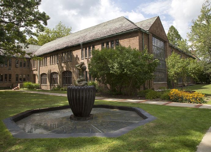 Exterior view of Cranbrook Academy of Art, featuring historic brick architecture, large glass windows, and a sculptural fountain set in a landscaped courtyard.