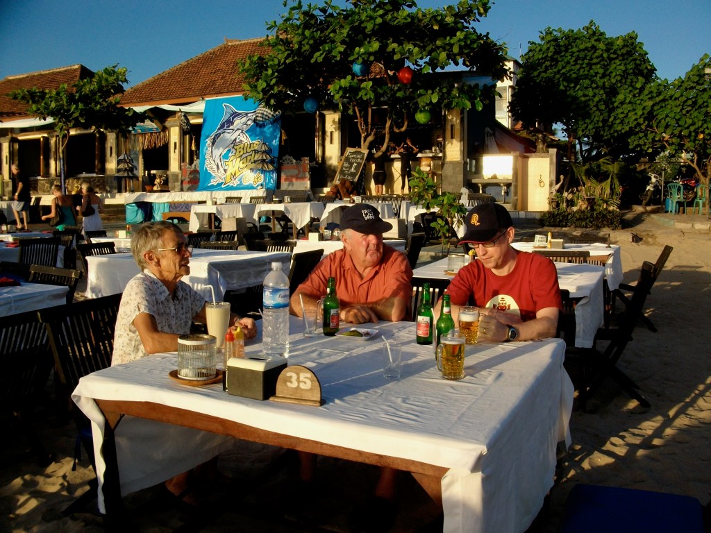 Author on Jimbaran Beach, Indonesia (Bali) seated at typical wooden holiday table and chairs.