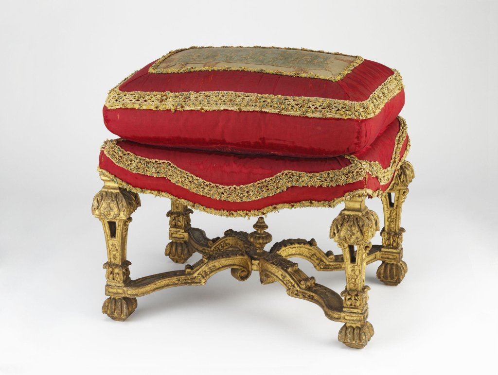 Stool of carved and gilt wood, upholstered with a valance of crimson velvet and a loose cushion of crimson silk velvet paned with two figured silk velvets