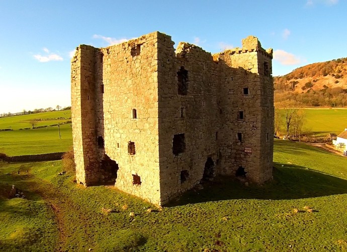 Ruined stone Arnside Tower, a medieval pele tower, standing in open green fields near Arnside, Cumbria, under a clear blue sky.
