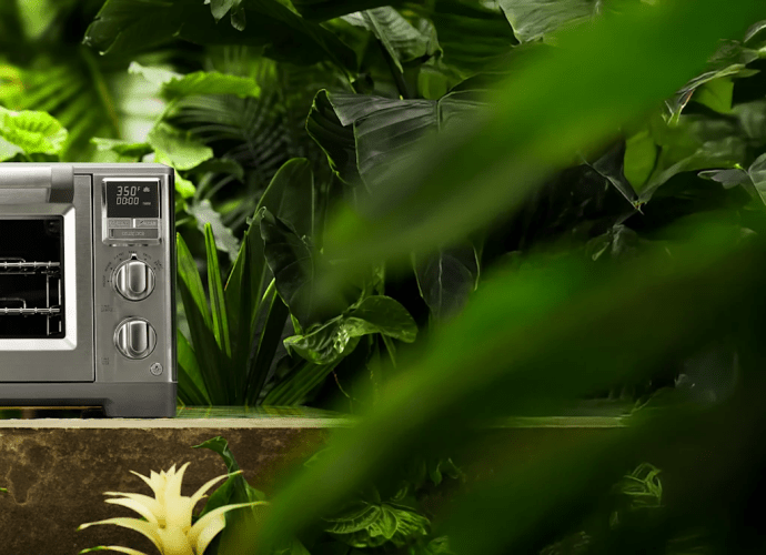 Lotus “The Perfectionist” stainless steel air fry and convection oven surrounded by lush green jungle foliage.