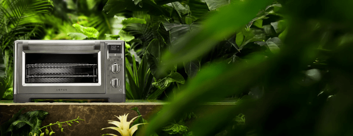 Lotus “The Perfectionist” stainless steel air fry and convection oven surrounded by lush green jungle foliage.