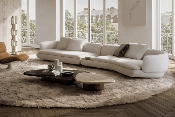 Minotti modular curved sofa in a soft neutral tone, styled with sculptural coffee tables and shag rug in a Parisian-inspired living room.