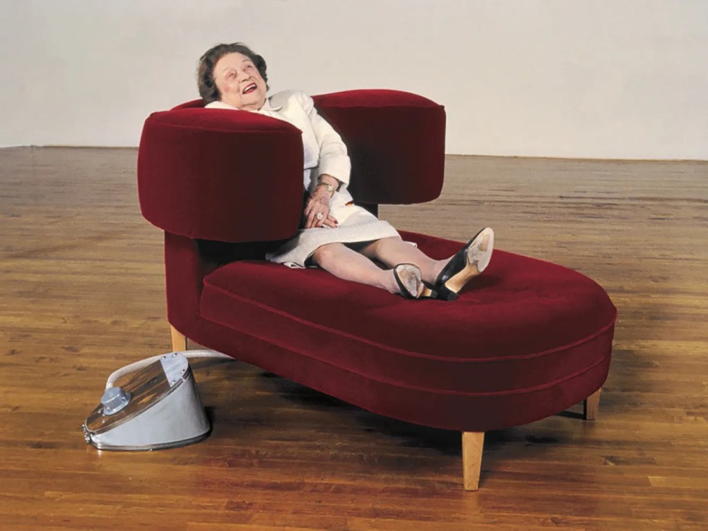 A woman relaxing in a red mohair Squeeze Chair designed by Wendy Jacob and Temple Grandin, with inflatable arms embracing her body.
