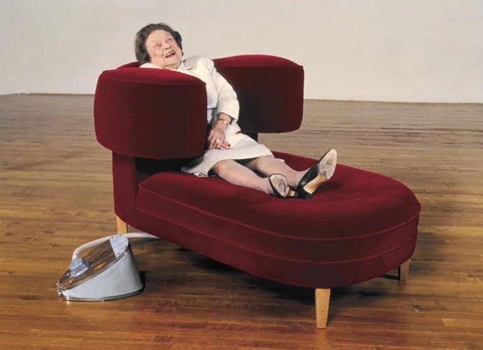 A woman relaxing in a red mohair Squeeze Chair designed by Wendy Jacob and Temple Grandin, with inflatable arms embracing her body.